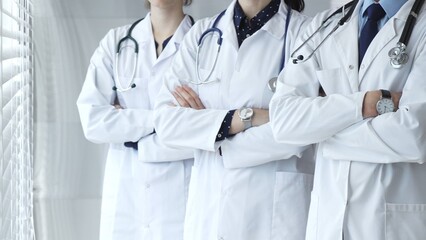 Doctors in white uniforms with stethoscopes stand together with folded hands, symbolizing unity, competence, experience, and dedication to the healthcare profession