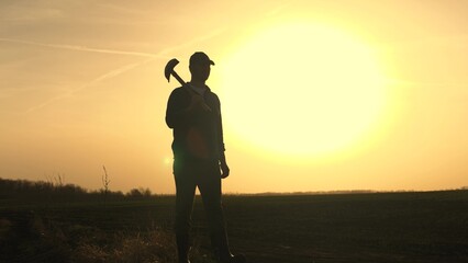 A farmer walks through the field with a shovel in rubber boots to dig the soil of the land at...
