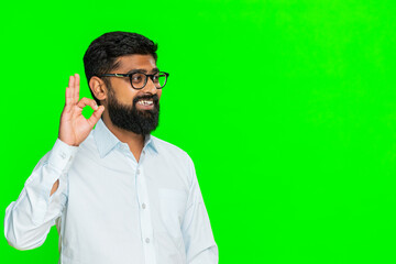 Indian man makes okay hand gesture with cheerful smile expressing agreement and positive attitude with friendly energy. Arabian guy isolated on green chroma key background showing approval and support