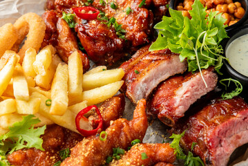 Assorted comfort food platter with barbecue ribs, chicken wings, onion rings, fries, dipping sauce, and garnish. Close-up, rustic presentation, ideal for food photography.