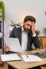 Middle-aged businessman at home office checks contracts spots error facepalms and marks fix with pen. Freelancer guy at table reviews legal text writes fix signs page and breathes relief after stress.