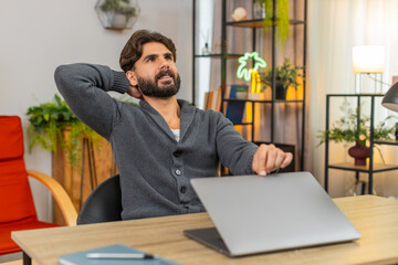 Indian man at home completes report on laptop checks lines presses send and exhales with relief work done ready to rest. Arabian guy at desk closes lid smiles quiet nod cleans workspace ends day calm