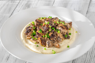 Braised meat and mushroom topping over creamy mashed potato served on white plate