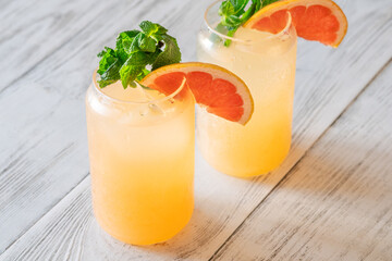 Two chilled Paloma cocktails with grapefruit slices and mint sprigs on white wood