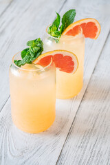 Two chilled Paloma cocktails with grapefruit slices and mint sprigs on white wood