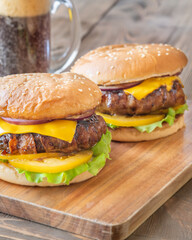 Two cheeseburgers with bacon beside dark stout on rustic wooden background