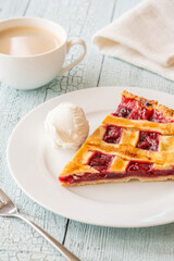 Cherry pie slice with melting ice cream and coffee on white plate