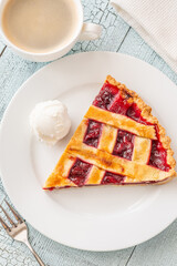 Cherry pie slice with melting ice cream and coffee on white plate