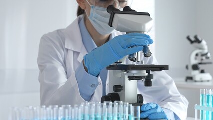 Scientist wearing protective gear carefully adjusting microscope lens, analyzing medical research samples with precision in sterile laboratory environment