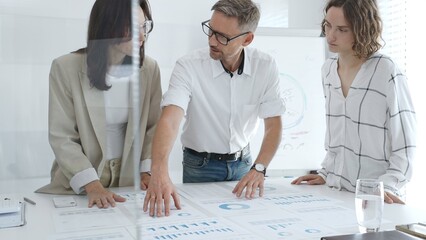 Professional team analyzing financial charts, colleagues reviewing data with focused expressions in modern workplace setting. Business people concept