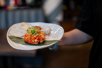 Gourmet appetizer served on a white plate with banana leaf, vegetable tartare, microgreens, bread slices, and creamy spread. Elegant restaurant presentation, selective focus.