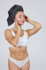 A young beautiful girl in white lingerie with a towel on her head does cosmetic procedures and closed her eyes.