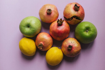 Fresh and colorful still life with ripe pomegranates, lemons, and green apples on a soft purple background. Modern food photography concept for healthy eating, freshness, and organic lifestyle themes 