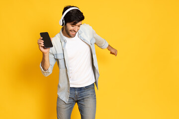 Young man listening favorite music on mobile phone application with wireless headphones and dancing, Top music chart concept