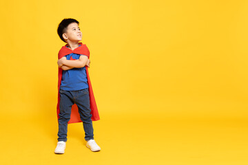 Asian little boy superhero standing and smiling with red cape isolated yellow background, Full body composition
