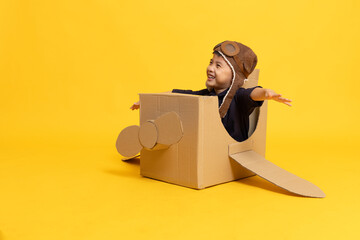 Asian little boy aviator playing with cardboard airplane isolated on yellow background, Kid toy diy concept