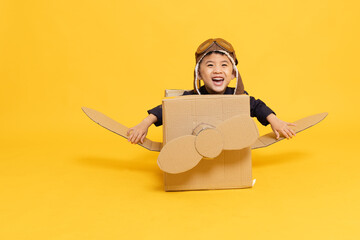 Asian little boy aviator playing with cardboard airplane isolated on yellow background, Kid toy diy concept