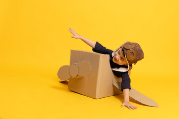 Asian little boy aviator playing with cardboard airplane isolated on yellow background, Kid toy diy concept