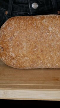 Woman Slowly Sliding Rustic Bread Loaf Forward on Wooden Cutting Board &mdash; Close Up