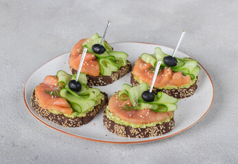 Sandwiches with salted salmon, black olives and cucumber on gray background