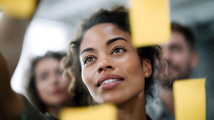 A woman collaborates with colleagues brainstorming ideas on a glass wall with sticky notes in a modern office setting