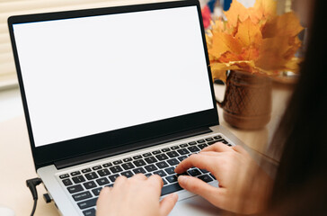 Woman working on laptop with blank screen at a desk in autumn, typing on keyboard.