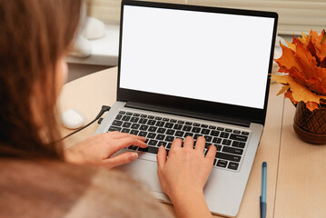 Woman working on laptop with blank screen at a desk in autumn, typing on keyboard.