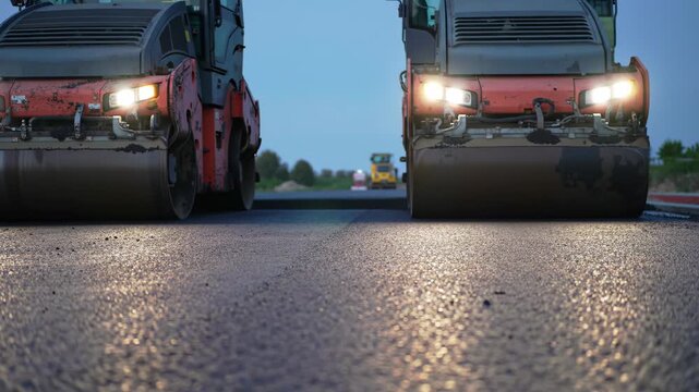 Two road rollers compacting asphalt at dusk, highway construction with machinery, industrial paving.