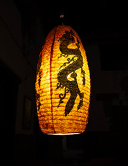 Traditional Asian hanging lantern with intricate black dragon design glowing warmly in the dark. Ideal for use in cultural, travel, interior, or oriental-themed design and editorial projects.