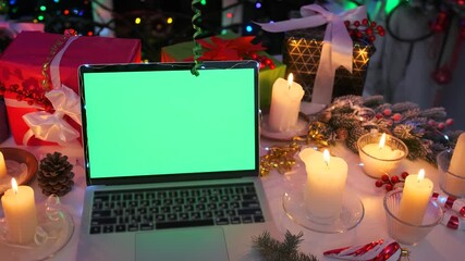 Festive laptop with green screen among Christmas candles, gifts, and pine cones on holiday table. Perfect mockup background for design and seasonal projects. - Powered by Adobe