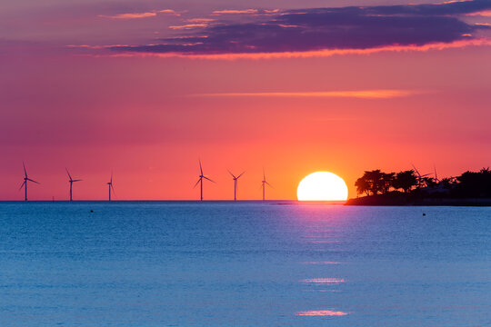 &Eacute;oliennes offshore au soleil couchant encore visible au dessus de l'horizon. Ciel orange et magenta. Parc &eacute;olien Yeu Noirmoutier
