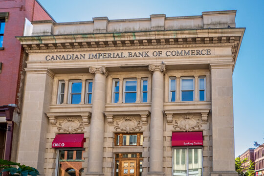 Saint John, NB - CA - Sep 30, 2025 A detailed view of the historic Canadian Imperial Bank of Commerce building with red awnings and classical columns under a clear blue sky.