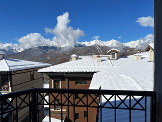Snow-covered rooftops of mountain lodges under bright blue sky with fluffy clouds, picturesque...