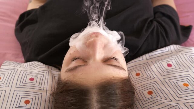 Young girl relaxes on bed while vaping at home during afternoon