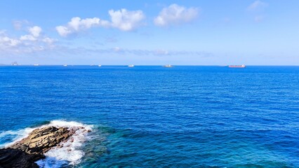 Atlantic Ocean view with cargo ships anchored offshore near Gran Canaria, Canary Islands, Spain. Bright blue sea, scattered clouds, and rocky coast under clear sunlight on a calm summer day.