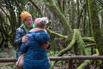 Active senior couple embracing enjoying winter excursion in a mountain forest with moss covered...