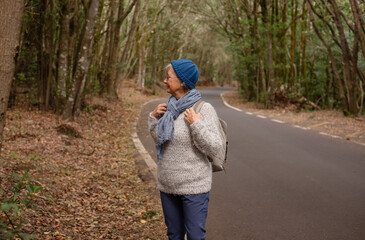 Senior caucasian woman on road trip with backpack on shoulders enjoying freedom and nature. Elderly active woman on a leisure activity, healthy lifestyle in retirement