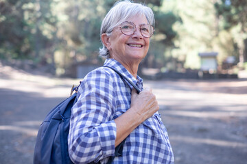 Smiling gray haired senior woman with backpack walking on a mountain hike enjoying free time and freedom in nature, senior retired and healthy lifestyle concept