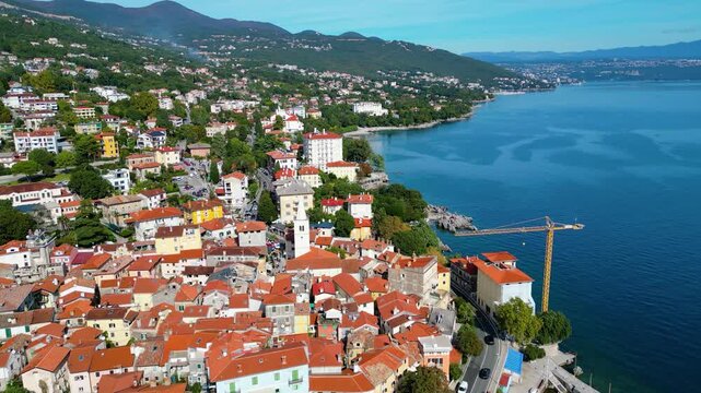 Scenic aerial view of the coastal town Lovran on the Opatija Riviera, Croatia, with red-roofed houses, Adriatic Sea, and green Učka mountain slopes in the background