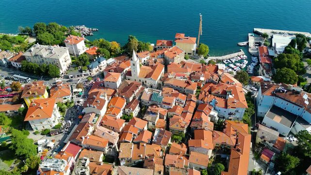 Scenic aerial view of the coastal town Lovran on the Opatija Riviera, Croatia, with red-roofed houses, Adriatic Sea, and green Učka mountain slopes in the background