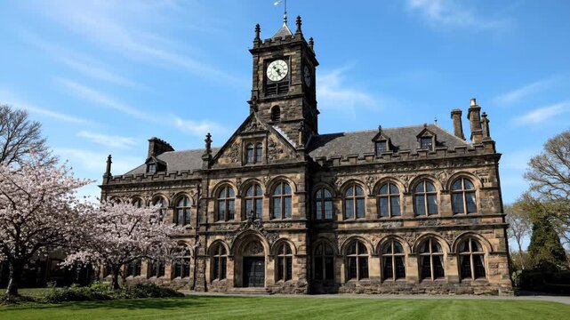 Historic stone building with clock tower and cherry blossom trees