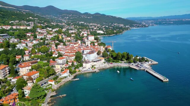 Scenic aerial view of the coastal town Lovran on the Opatija Riviera, Croatia, with red-roofed houses, Adriatic Sea, and green Učka mountain slopes in the background