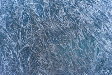 Close-up of blue frosty glass covered with sharp, sparkling ice crystal patterns. The composition...