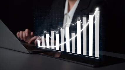 A business professional works intently on a laptop, while a digital growth graph emerges, symbolizing analysis and strategic financial success in a modern workspace. Copula