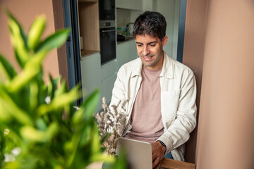Smiling Hispanic man teleworking from home on a balcony