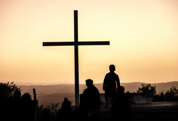 Cross with people in shadow over the Lourdes Grotto in Villa Giardino, Córdoba. At dusk with the village lights on. With copy space. © Uri Gordon