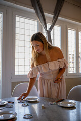 Woman arranging plates on dining table in bright room with sunlight