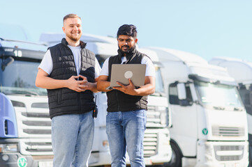 Logistics managers using laptop standing by trucks