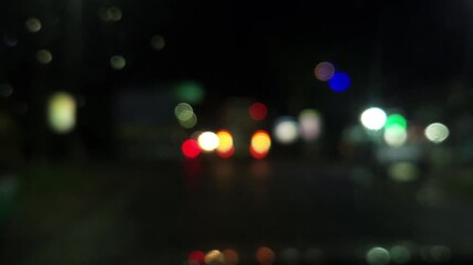 Out-of-focus headlights and taillights illuminate the dark city road at night, forming beautiful circular bokeh patterns that capture the mood of urban traffic and motion.