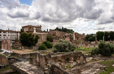 Ancient Roman Forum ruins with historic buildings and green trees under cloudy sky